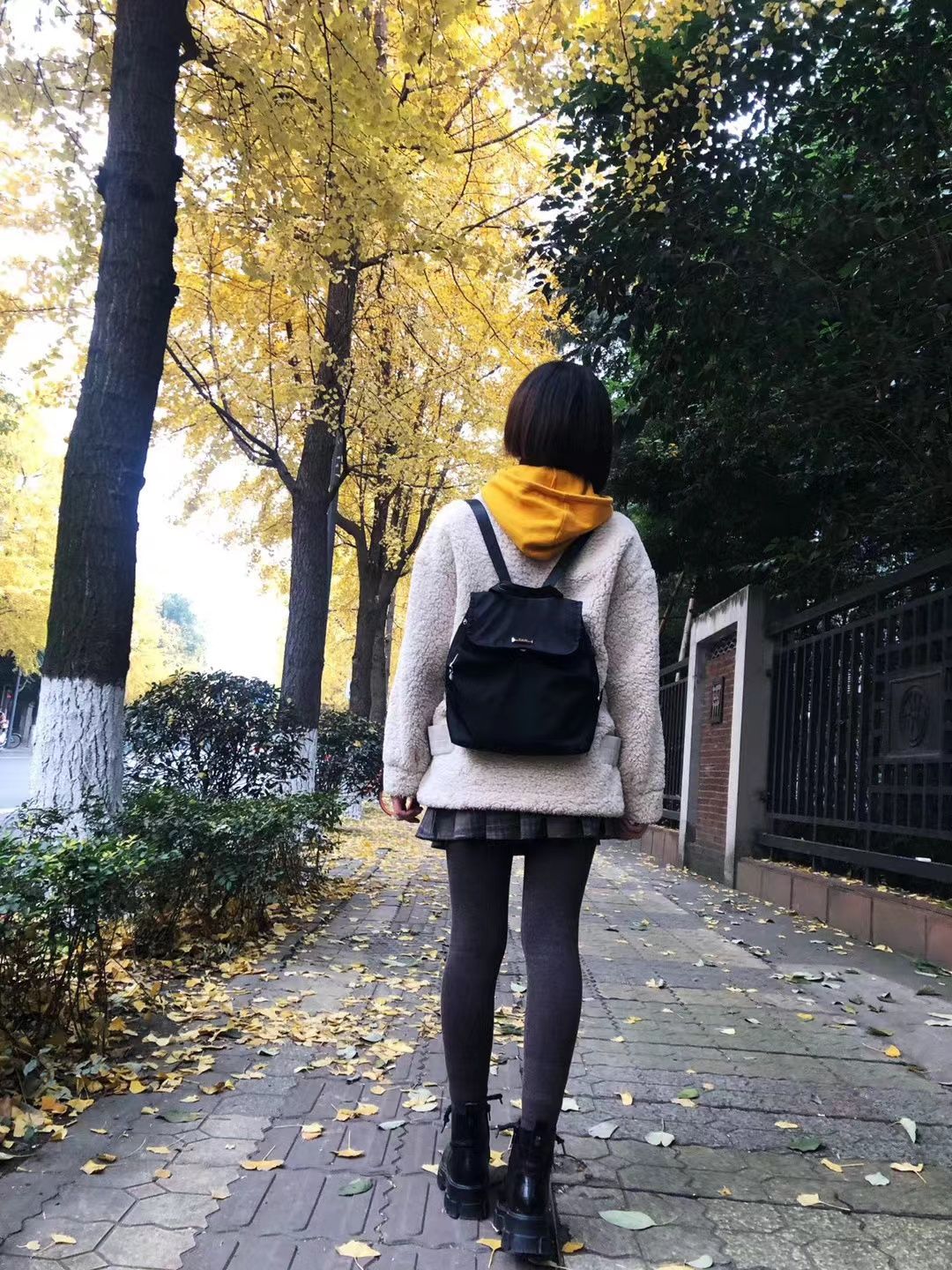 Miya with her back turned to the camera, on a sidewalk in the fall