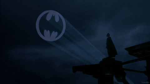 Batman is staring the at the bat signal, a white light with a bat symbol appearing.