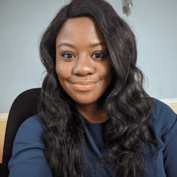 Sarah Chima, a young-looking Black woman, smiling for the camera while sitting in a chair.