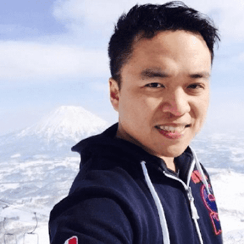 Shawn Wang, a young-looking Asian man, smiling for a selfie with a snow-capped mountain in the background.
